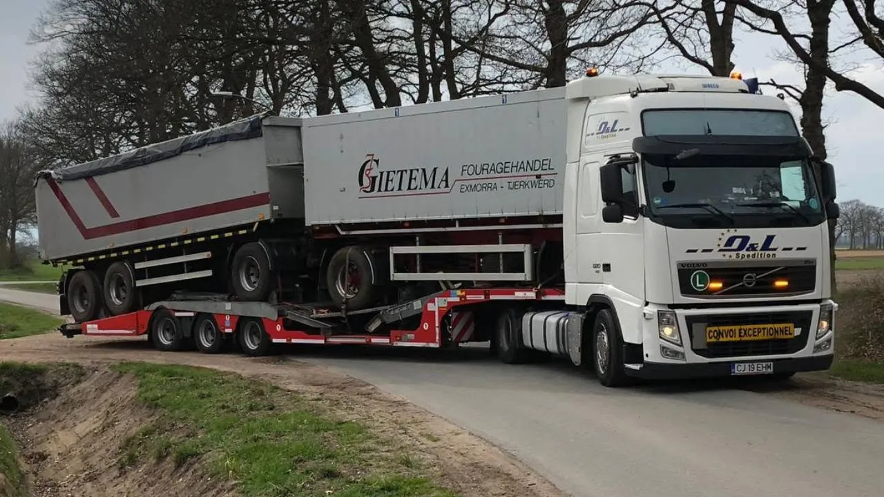 Semiremorcă basculantă transportată ca marfă pe trală, pe un drum de țară din Olanda. Ansamblul circulă cu placa de convoi excepțional. - OL Speditionwagon